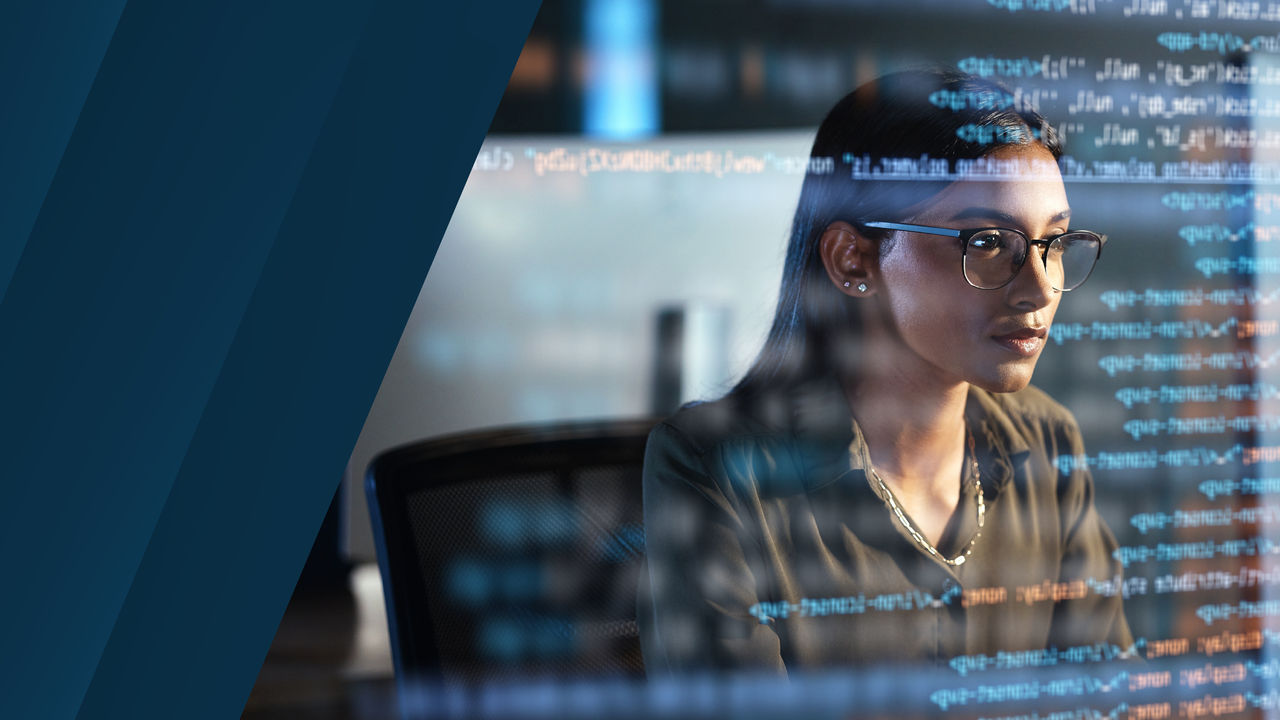 Woman wearing glasses focused on computer code reflected on a screen, symbolizing technology and data analysis.