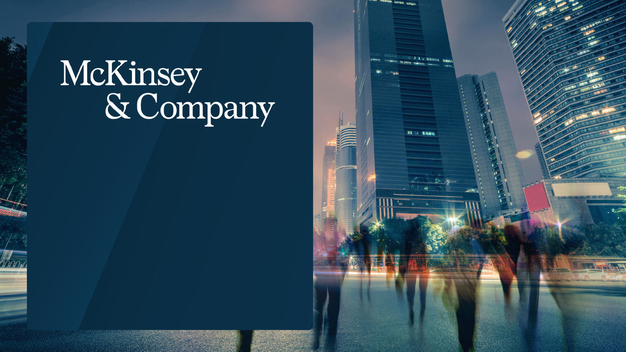 McKinsey & Company logo on a dark blue panel, set against a cityscape with illuminated skyscrapers and blurred silhouettes of people walking at night.