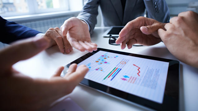 4 sets of hands belonging to business men planning over a tablet with graphs showing growth
