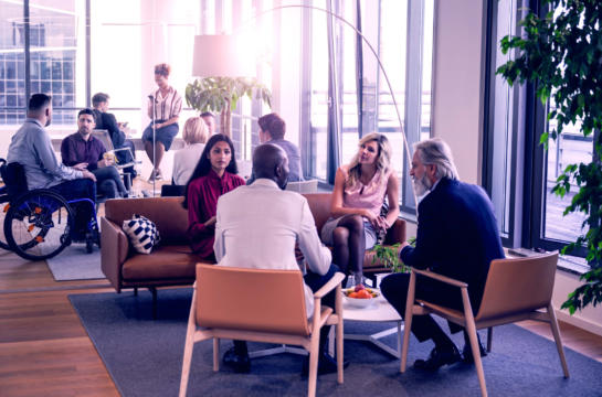 A diverse group of coworkers engaged in a casual meeting in an open floor plan